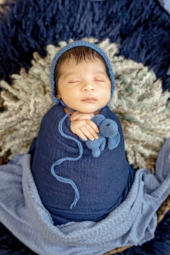 Close portrait of sleeping baby swaddled in navy wrap, surrounded by fuzzy blanket.