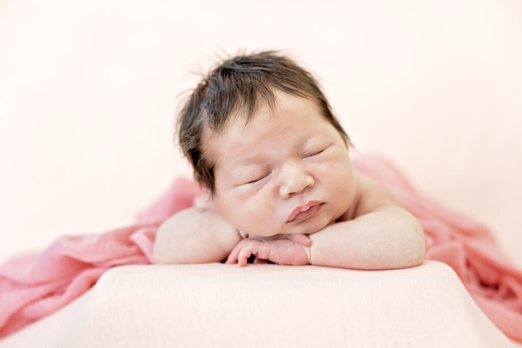 Close-up of a baby girl in pastel pink wrap, tiny eyelashes visible as she sleeps.