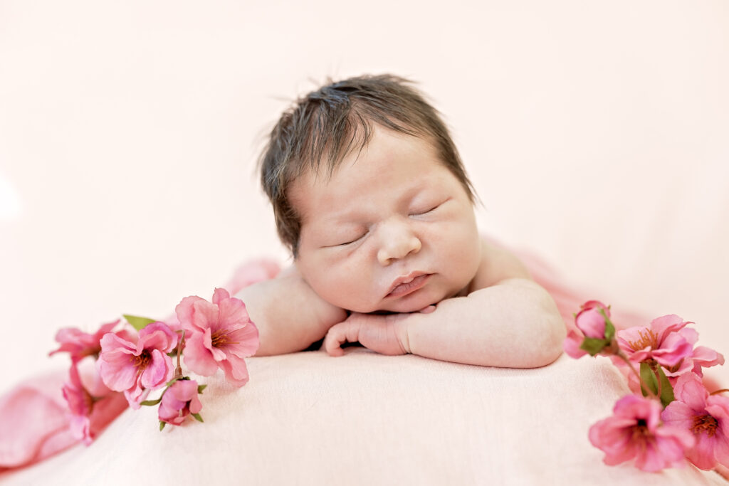 Overhead shot of newborn swaddled in blush tones, eyes closed and relaxed.