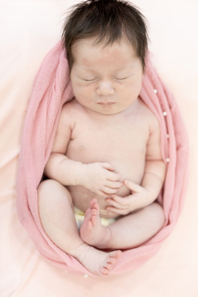 Baby girl posed in a light pink wrap, curled up and sleeping soundly.