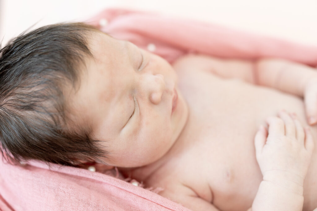 Close-up side view of newborn girl on pink blanket, peaceful and serene.