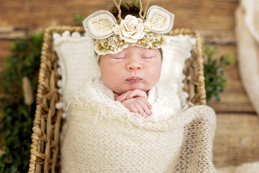 Baby sleeping on cream fabric with tiny lace wrap and greenery details.