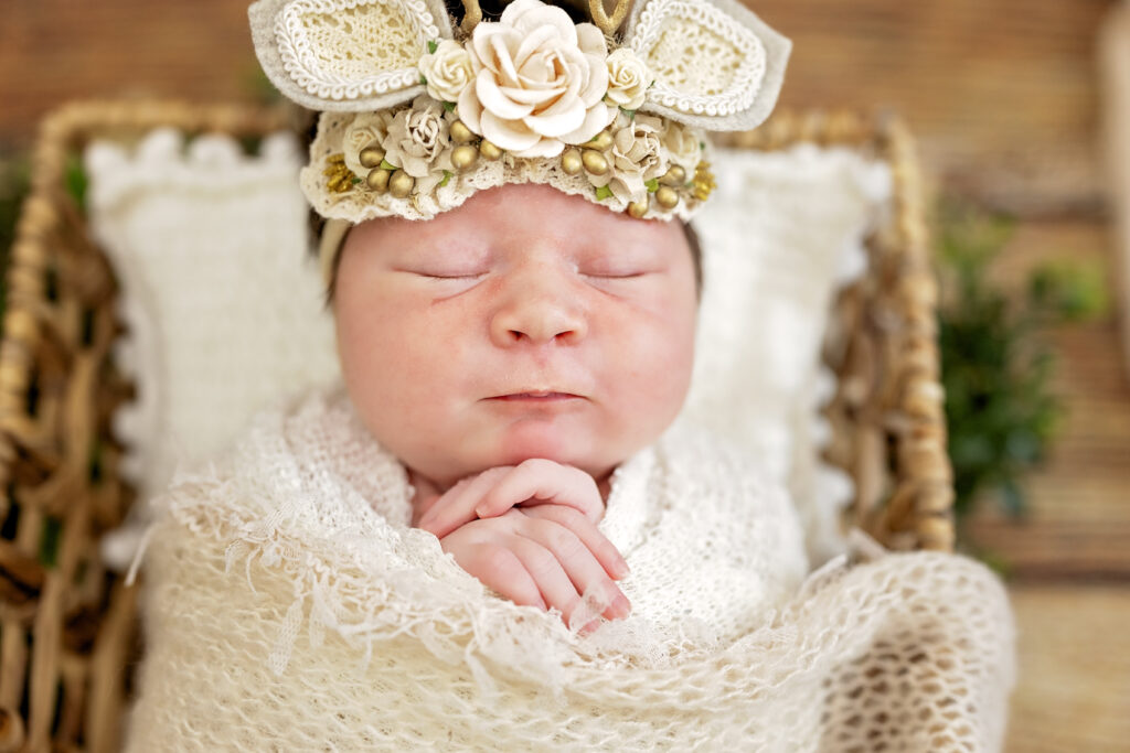 Newborn girl in ivory wrap, sleeping in basket with subtle floral touches