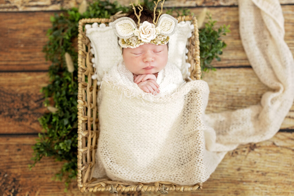 Close-up of sleeping newborn wrapped in cream tones, rustic wood background.