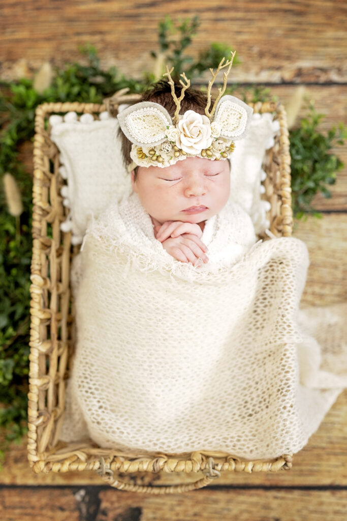 Newborn girl posed in shallow wooden bowl, wrapped in neutral beige fabric.