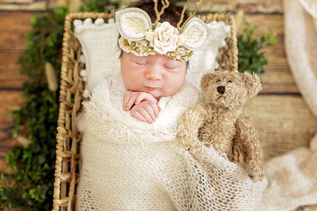 Wide-angle shot of newborn in cream lace wrap with green foliage accent.