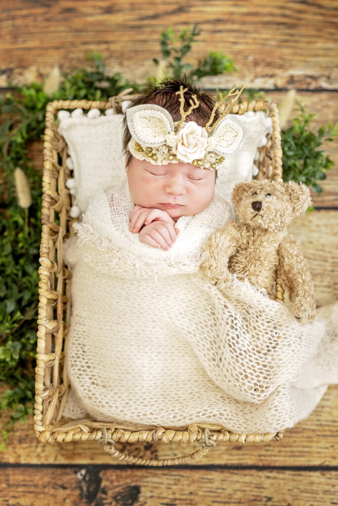 Baby swaddled in soft neutrals, nestled in rustic basket on wood plank floor.