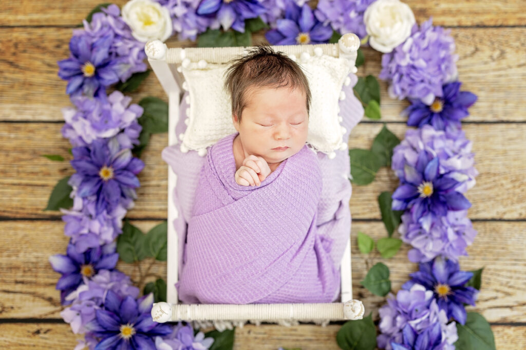 Close-up of newborn in lavender wrap and purple flower crown.