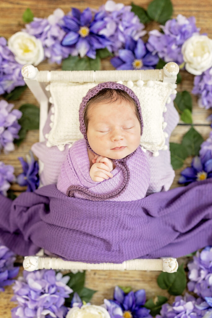 Close-up of peaceful newborn girl swaddled in purple wrap with floral details.