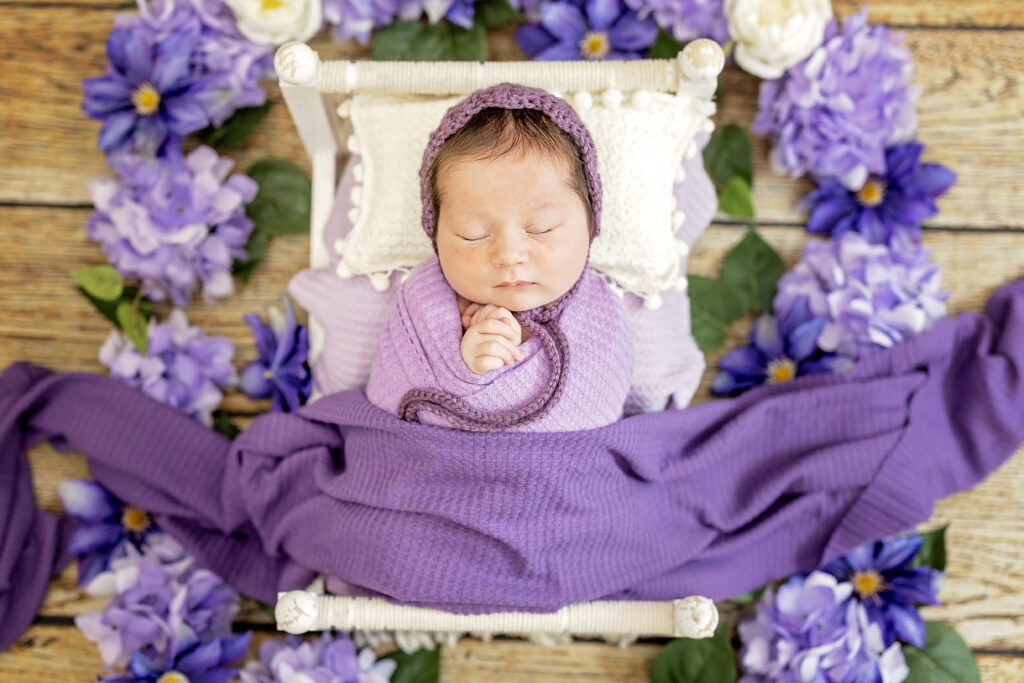 Newborn girl wrapped in bright pink tulle, resting in wooden basket.