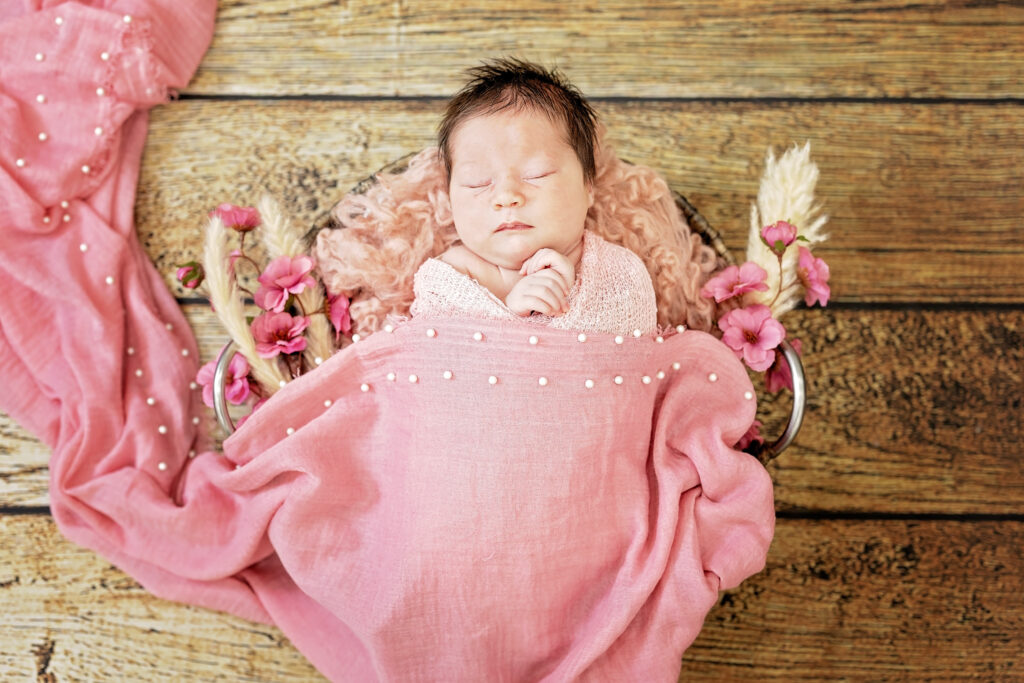 Baby wrapped in soft pink fabric surrounded by matching pink flowers.
