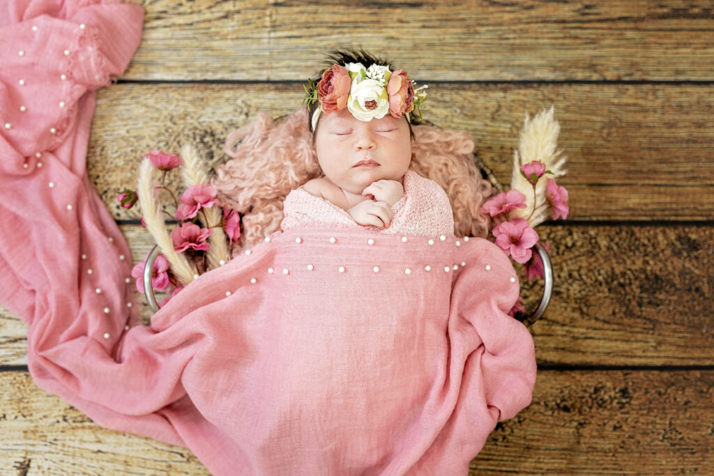 Newborn girl on wooden floor, pink tones and delicate newborn pose.