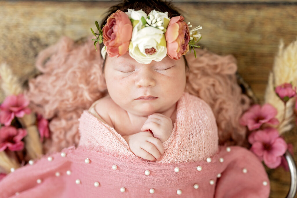 Baby wrapped in rose-pink fabric, small hands peeking out under chin.