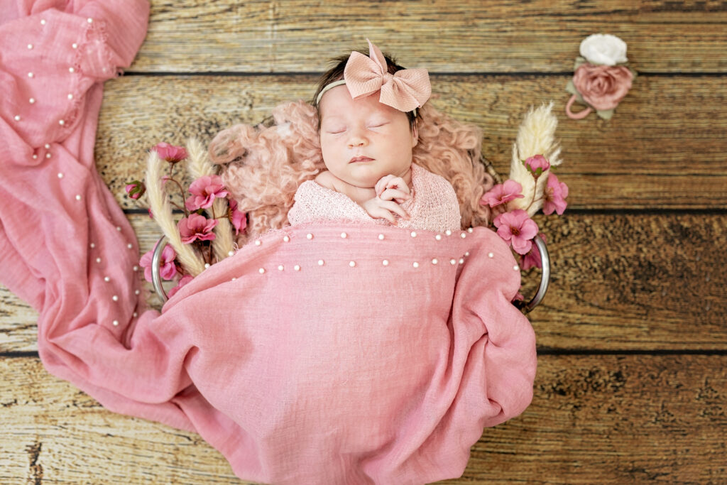 Sleeping newborn swaddled in pink wrap on rustic backdrop, soft natural light.
