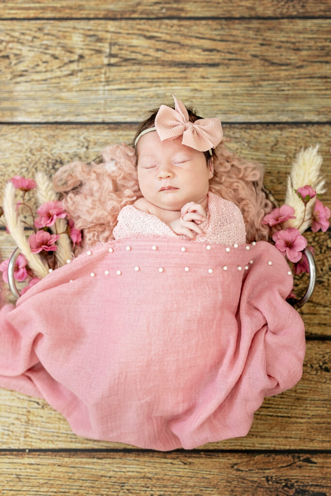 Overhead shot of baby girl in pink tulle wrap with floral background.