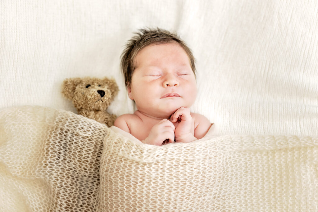 Newborn girl swaddled in cream tones, resting on a soft white blanket.
