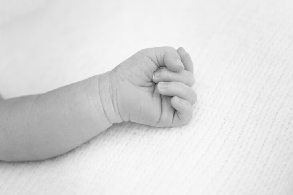 Black-and-white macro of newborn’s curled fingers.