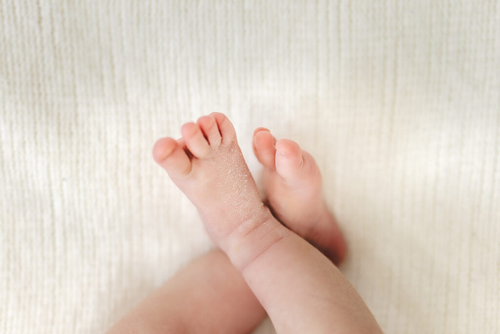 Baby’s tiny foot resting on soft cream blanket, newborn detail photo.