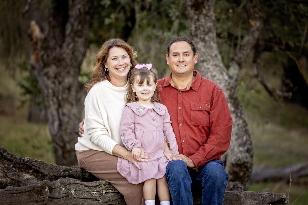 Family sitting on a log smiling at the camera, oak trees in background