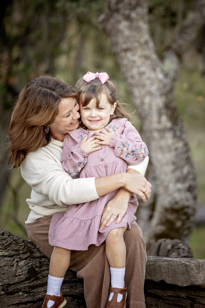 Mom kissing daughter on the cheek during a warm embrace on a log at Jim Green Trail