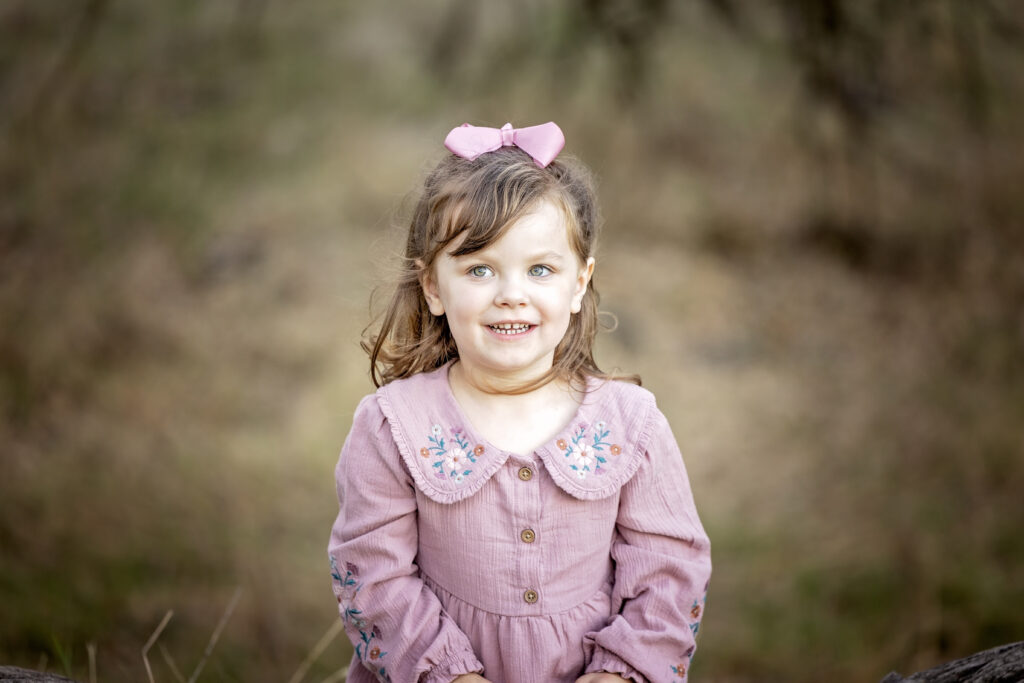 Close-up portrait of a young girl in a pink dress with embroidered collar, smiling softly