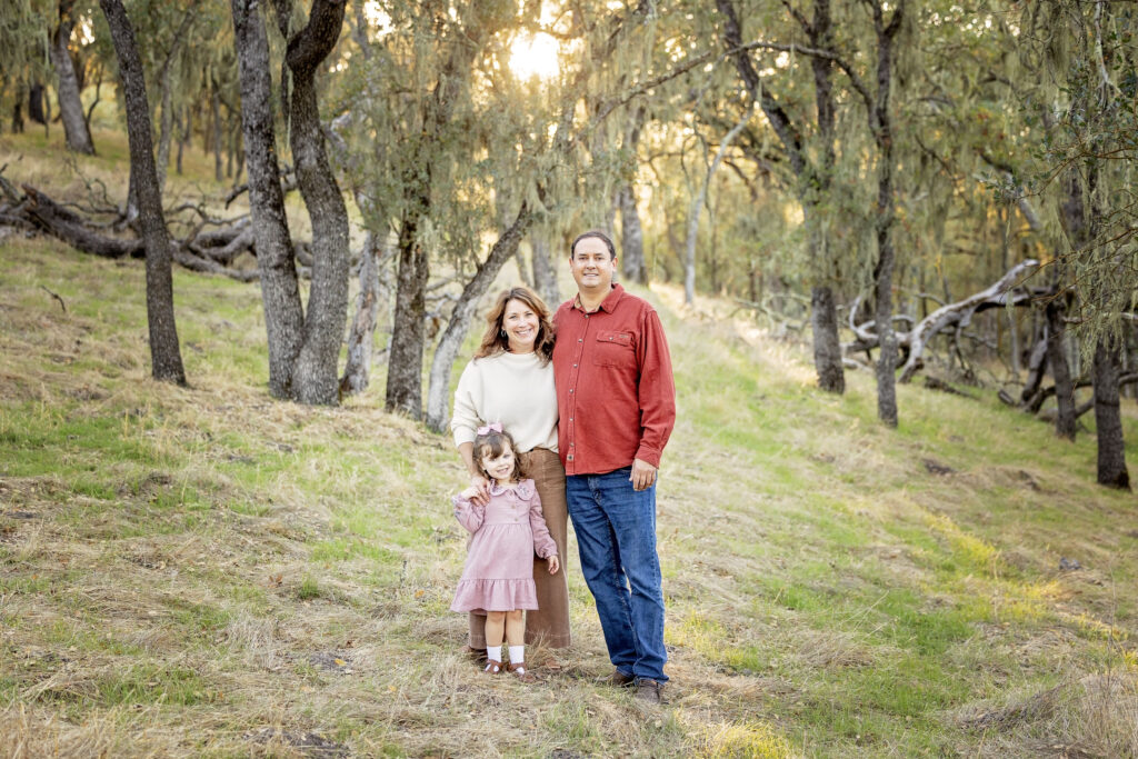 Family standing on a grassy trail surrounded by oak trees with sunlight streaming through at Jim Green Trail