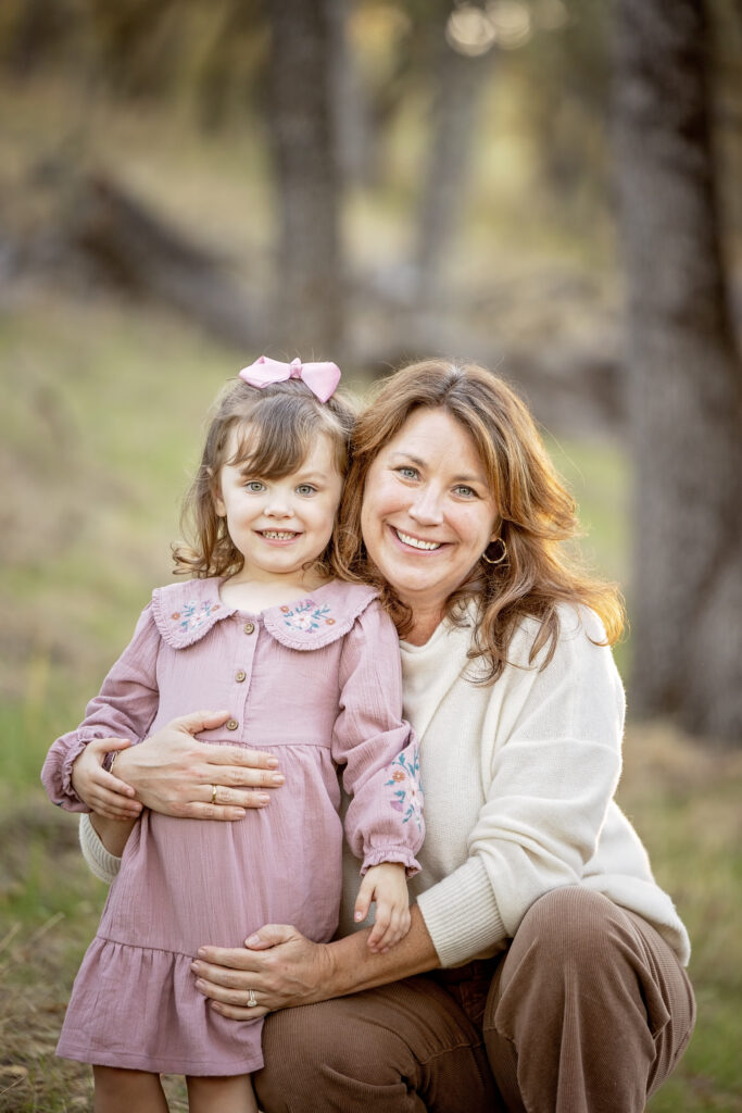 Mom and daughter sitting together and smiling at the camera during a golden hour shoot in Atascadero
