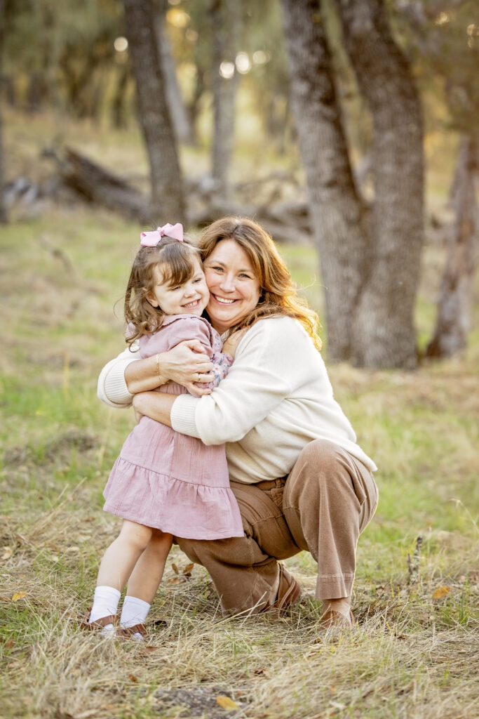 Mom smiling while holding daughter on her lap in a tender moment during their family photo session