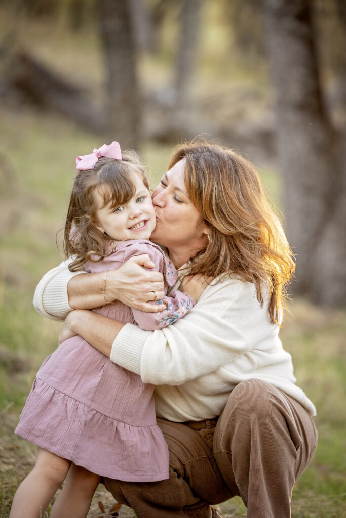 Daughter receiving a kiss on the cheek from mom while sitting in the grass at Jim Green Trail