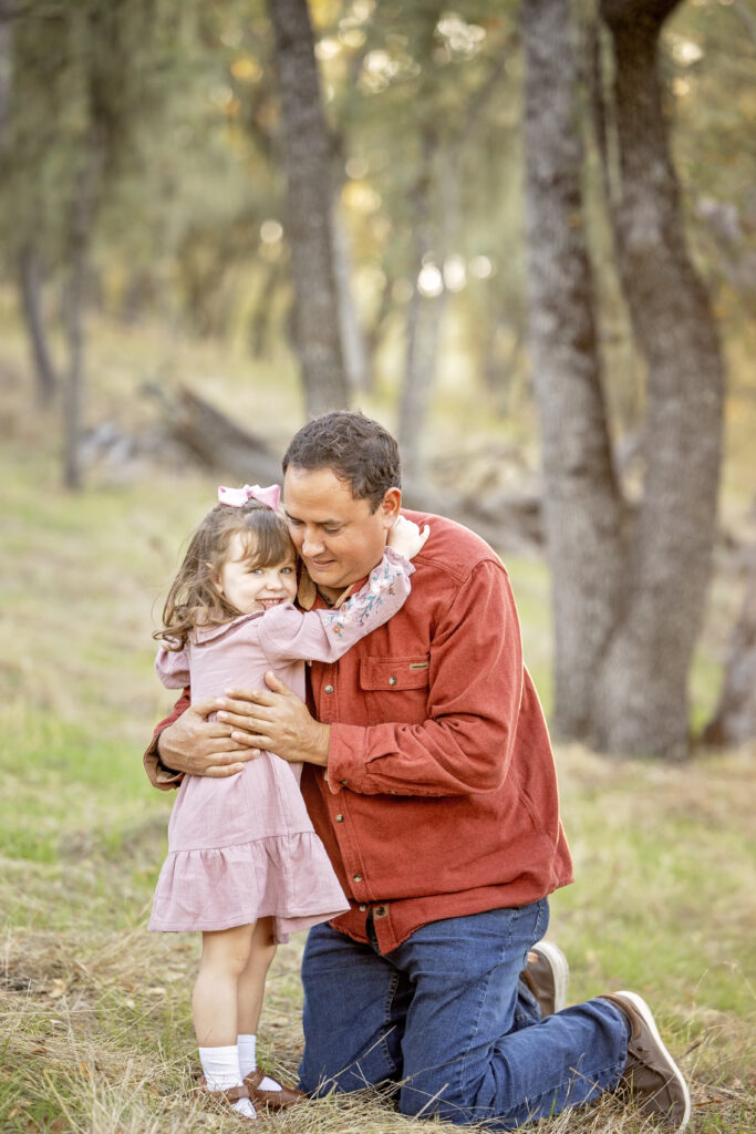 Little girl hugging her dad with a big smile, surrounded by trees and soft sunset light